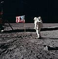 Three astronauts in spacesuits without helmets sitting in front of a large photo of the Moon.